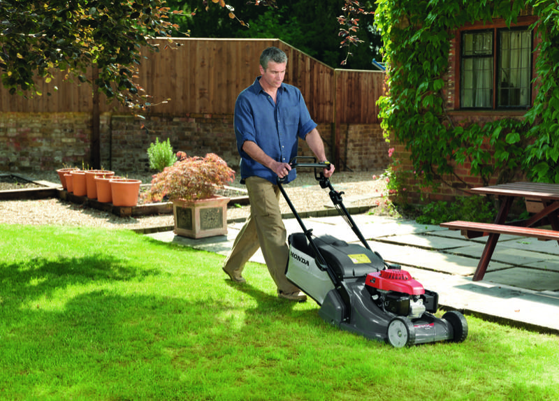 Man using Honda HRX mower to cut the lawn in front of the house.